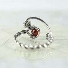 A special silver and garnet ring with a twist and open spiral design. It's adjustable and perfect as a gift if you're not quite sure of the size you need. The shank is twisted from one wire and in the loop at the end is nestled an AA-plus faceted wine red garnet bead and the opposite ends are shaped into spirals. Both twists and spirals are classic and has been used since Celtic times in jewellery. I think my Danish heritage is shining through. :o) Garnet is a stone of positive thoughts which is Red Adjustable Wire Wrapped Rings, Adjustable Red Wire Wrapped Rings, Adjustable Red Spiral Jewelry, Handmade Adjustable Ruby Ring, Handmade Adjustable Silver Ruby Ring, Adjustable Silver Ruby Ring, Celtic Ring, Celtic Rings, Jewellery Silver