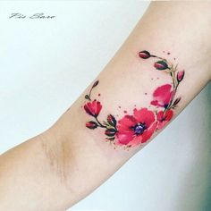 a woman's arm with red flowers on it and watercolor paint splatters