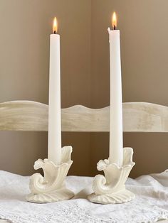 two white candles sitting on top of a bed