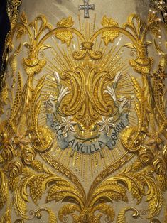 the back of a dress with gold embroidered on it and an ornate cross in the center