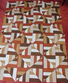 a very large quilt on the floor with red and brown colors, it looks like an abstract pattern