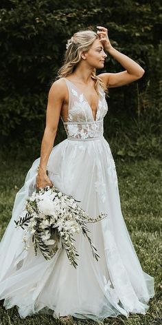 a woman in a white wedding dress holding a bouquet and looking at the camera with her hand on her head