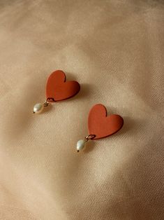 two red heart shaped earrings with pearls hanging from them on top of a white cloth