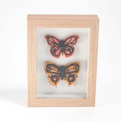 two butterflies in a wooden frame on a white background, one is orange and the other is black