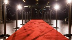 a red carpet is lined up between two metal poles with lights on them at night