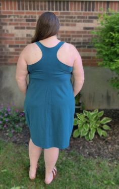 a woman standing in front of a brick building wearing a blue dress and flip flops