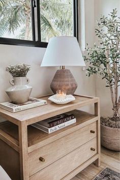 a table with a lamp on it next to a potted plant and a window