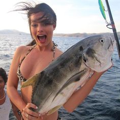 a woman holding a large fish while standing on a boat with another man in the background