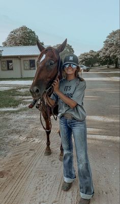 a girl is standing next to a horse on the dirt road with her hat on