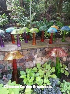 colorful glass umbrellas are lined up on the side of a brick wall in a garden