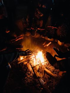 people sitting around a campfire with their hands on the fire and one person reaching for something