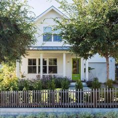 a white house with trees in front of it and a wooden fence around the yard