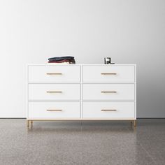 a white dresser with gold handles and drawers in an empty room next to a wall