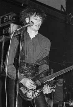 black and white photograph of a man playing an electric guitar in front of a microphone