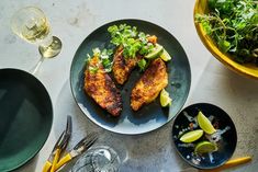 two plates with food on them next to glasses and utensils, one has lemon wedges