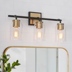 three light bathroom fixture with clear glass shades and gold trim on the mirror above it