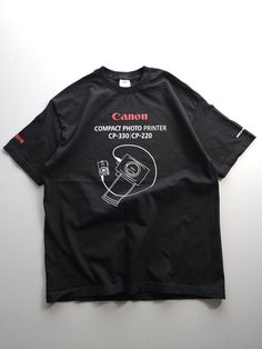 a black t - shirt with the canon logo on it is laying on a white surface