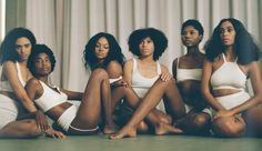 four women in white bathing suits sitting on the floor with their arms around each other