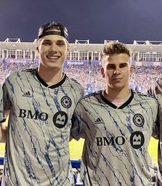 two men standing next to each other in front of a stadium