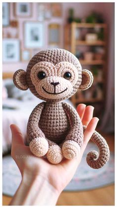 a small crocheted monkey sitting on top of someone's hand in front of a bed