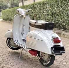 a white scooter parked on the side of a road next to a hedge