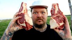 a man holding up two pieces of meat in front of his face with tattoos on both hands