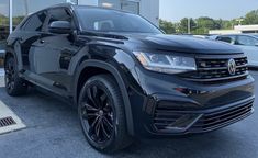 a black volkswagen suv parked in front of a dealership with other cars behind it