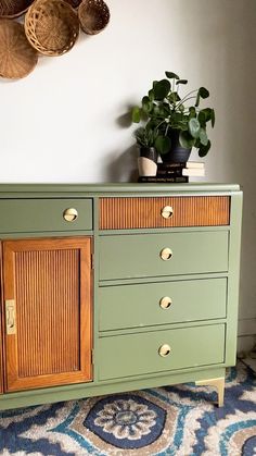 a green dresser with wooden drawers and baskets on the wall above it, along with a potted plant