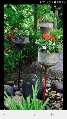 three metal planters filled with flowers on top of rocks