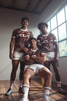 three men are posing for a photo in matching jerseys and shorts, one is holding a baby