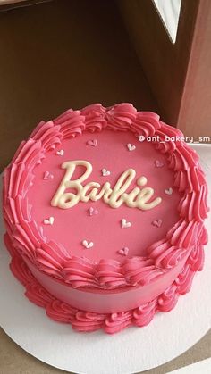 a pink cake with the word barbie on it is sitting on a table next to a box