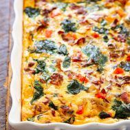 an egg casserole with spinach and bacon in a white dish on a wooden table