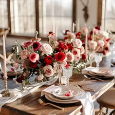 the table is set with white and red plates, silverware, and pink flowers