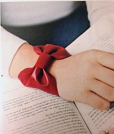 a person is reading a book with a red bow on their wrist and holding an open book