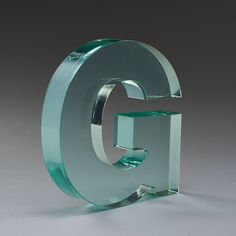 the glass letter g is on display in front of a gray background and grey backdrop