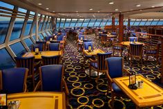 a dining area on a cruise ship with blue chairs and yellow tablecloths, looking out onto the ocean