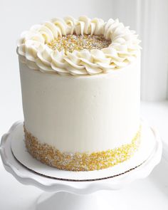 a cake with white frosting and gold sprinkles sitting on a plate