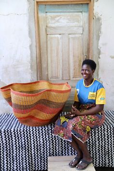 a woman sitting on top of a bench next to a large woven basket in front of a door