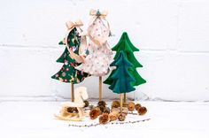 three wooden christmas trees with pine cones and bows on them, sitting in front of a white brick wall