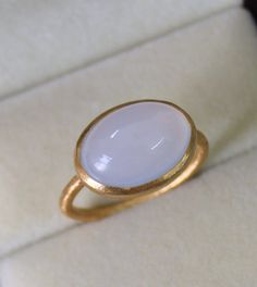 a gold ring with a white stone in it sitting on a velvet cushioned surface