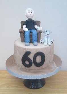 a birthday cake with an old man sitting on a chair and two dogs next to him