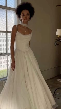 a woman standing in front of a window wearing a white dress with a high neck