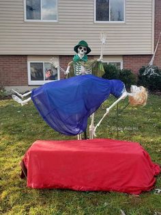 two fake skeletons sitting on top of a red blanket in front of a house with a blue sheet draped over it