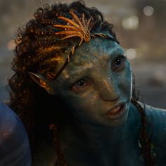 a woman with blue paint on her face and hair is staring at the camera while she's covered in mud