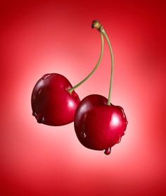 two cherries on a red background with drops of water falling off the cherries