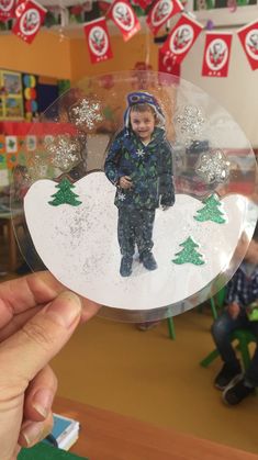 a hand holding up a glass ornament with a photo of a child on it