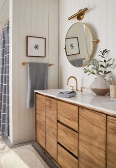 a bathroom with white walls and wood cabinets, a round mirror above the sink, and a gold faucet