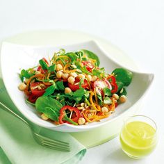 a white bowl filled with salad next to a glass of orange juice