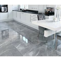 a modern kitchen with marble floors and white cabinetry is pictured in this image, there are two gray chairs at the table