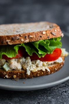 a sandwich with lettuce, tomato and chicken salad on a gray plate sitting on a table